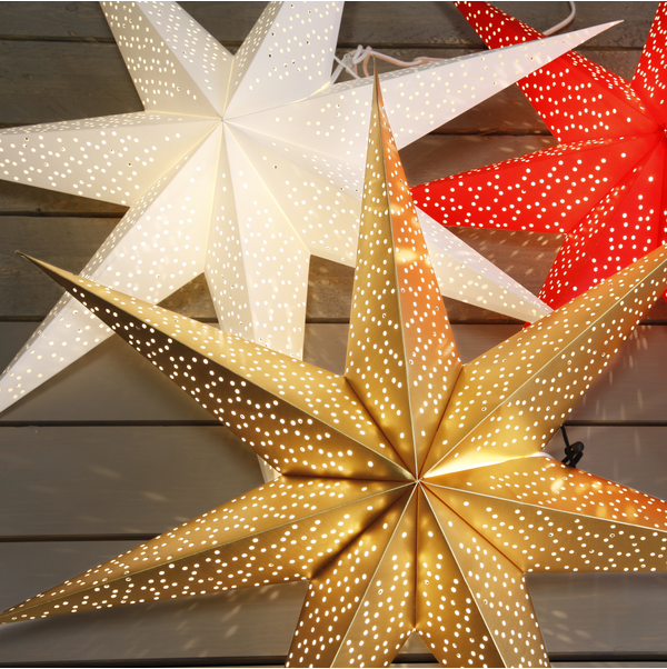 The Light: Star Trading - Paper Dot Star, Gold 27.5" lantern, with its perforated star-shaped design in white, gold, and red, creates a cozy atmosphere when placed on a wooden surface, making it perfect for indoor use.