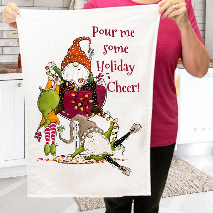 A person holds a "Christmas Pour Holiday Cheer" tea towel, made of cotton terry cloth, adorned with playful gnomes and the phrase "Pour me some holiday cheer!" which enhances the farmhouse decor.