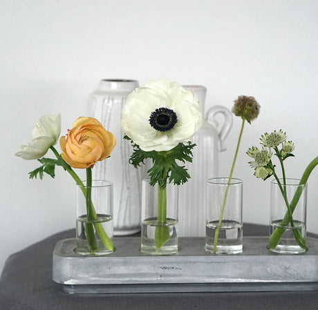 Two mini vases from the Stumpastaken Candleholder 2-pack hold vibrant flowers on a gray tray, creating a lovely table decoration with ceramic pitchers and the classic Stumpastaken in the background.