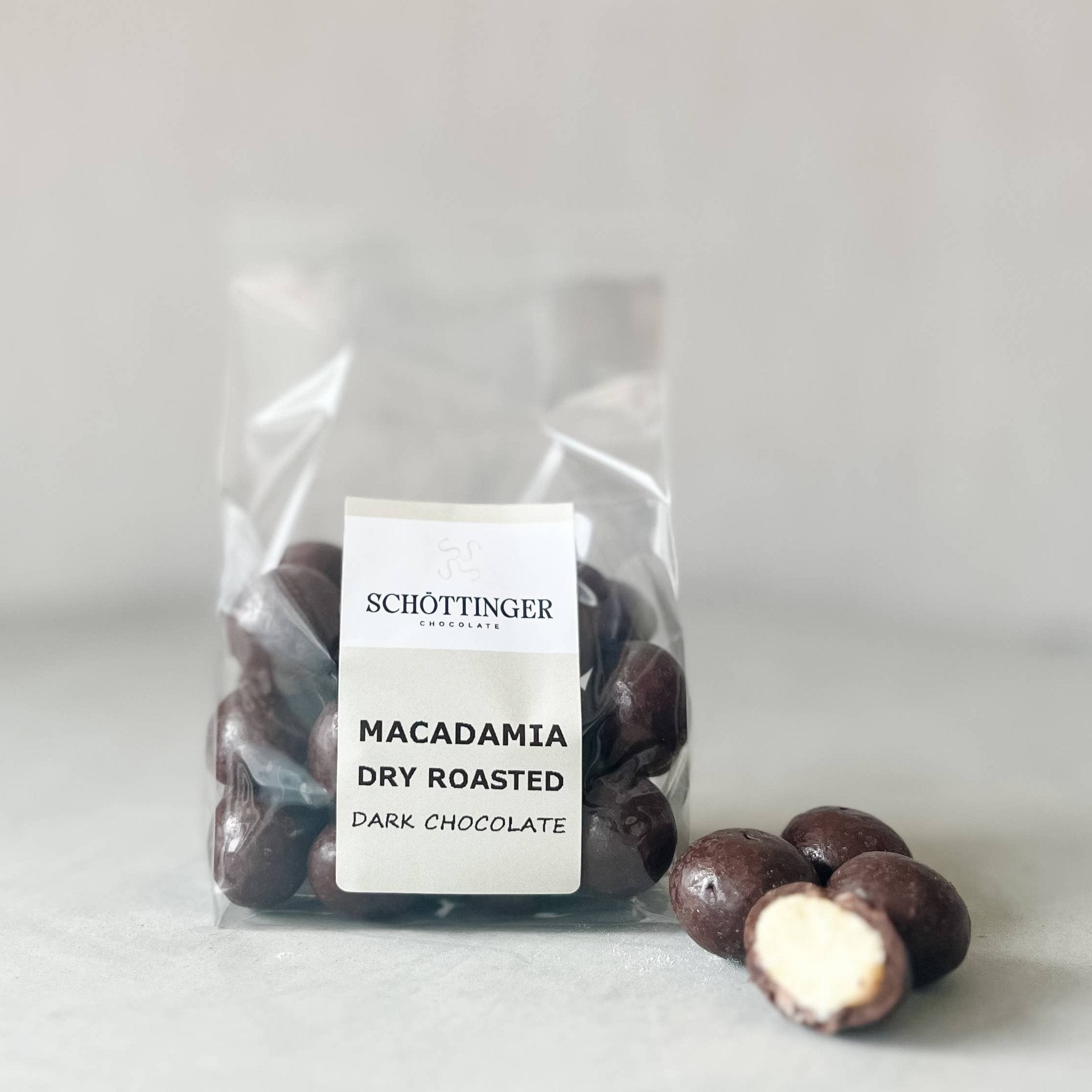 A bag labeled Macadamia Dark Chocolate, featuring handmade macadamia nuts from Sweden, with several chocolate-coated treats beside it.