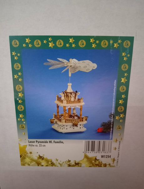 A Christmas-themed box showcases the Marketplace24 Pyramid: Christmas Pyramid Nativity Square with a manger scene at the base and four angels with horns on the top, standing 13 inches tall. The decorative wooden pyramid, featuring spinning blades and nativity figures, is set against a blue background framed with green borders and gold stars. Product text and a barcode are displayed at the bottom.