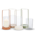 Four 10.5" Cylinder Lantern glass candle holders with metal bases in various colors, including one holding a lit white candle, create delightful outdoor decor accents.