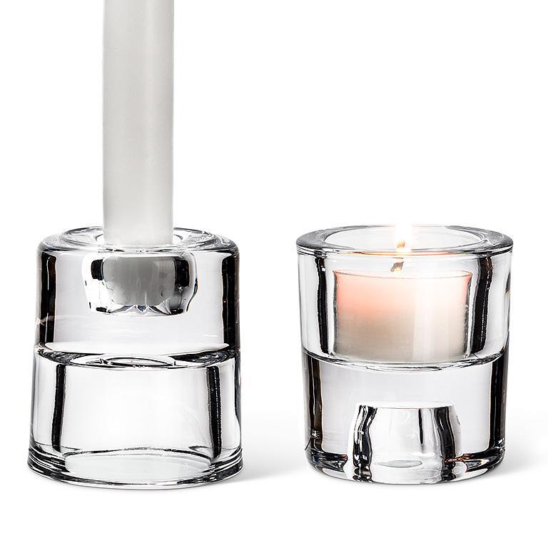 Discover the versatility of the 2.5" Glass Reversible Taper/Tealight Holder: one holder elegantly displays a tall white taper candle, while the other casts a warm glow with a lit white votive candle. These adaptable designs provide sophisticated lighting for any setting.