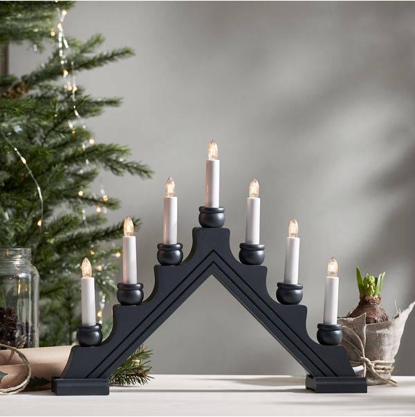 The Karin Gray 7 Light Candelabra, a traditional Swedish Christmas decoration with seven electric candles, graces the table alongside a small decorated Christmas tree and potted plant, perfect for indoor use.