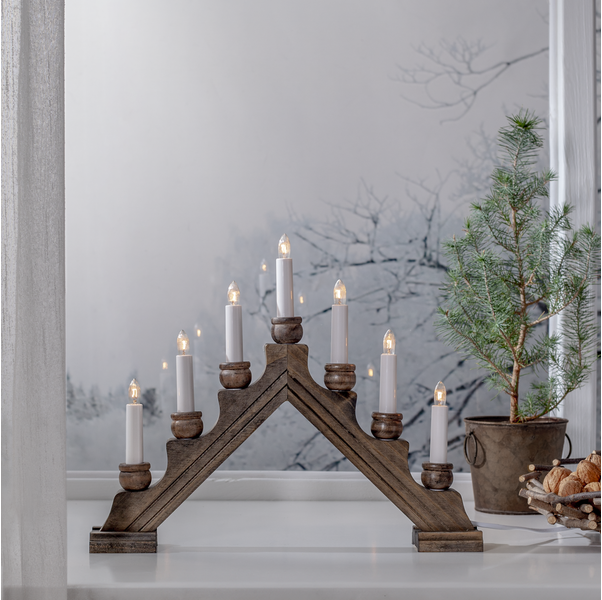 The Star Trading - Karin Electric 7-Light Candelabra from Sweden, with its seven lights, adorns a white surface beside a small potted evergreen against a backdrop of frosty windows.