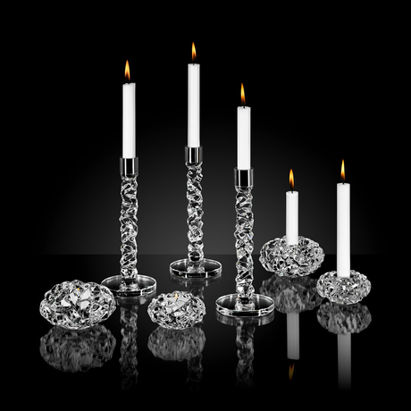 Six white candles, three tall and three short, in Orrefors crystal candle holders arranged on a reflective black surface.