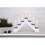 A Star Trading Ada White Electric 7-Light Candelabra sits on a table beside a potted pine arrangement and scattered pinecones.
