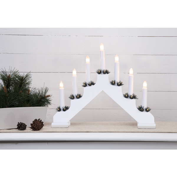 A Star Trading Ada White Electric 7-Light Candelabra sits on a table beside a potted pine arrangement and scattered pinecones.