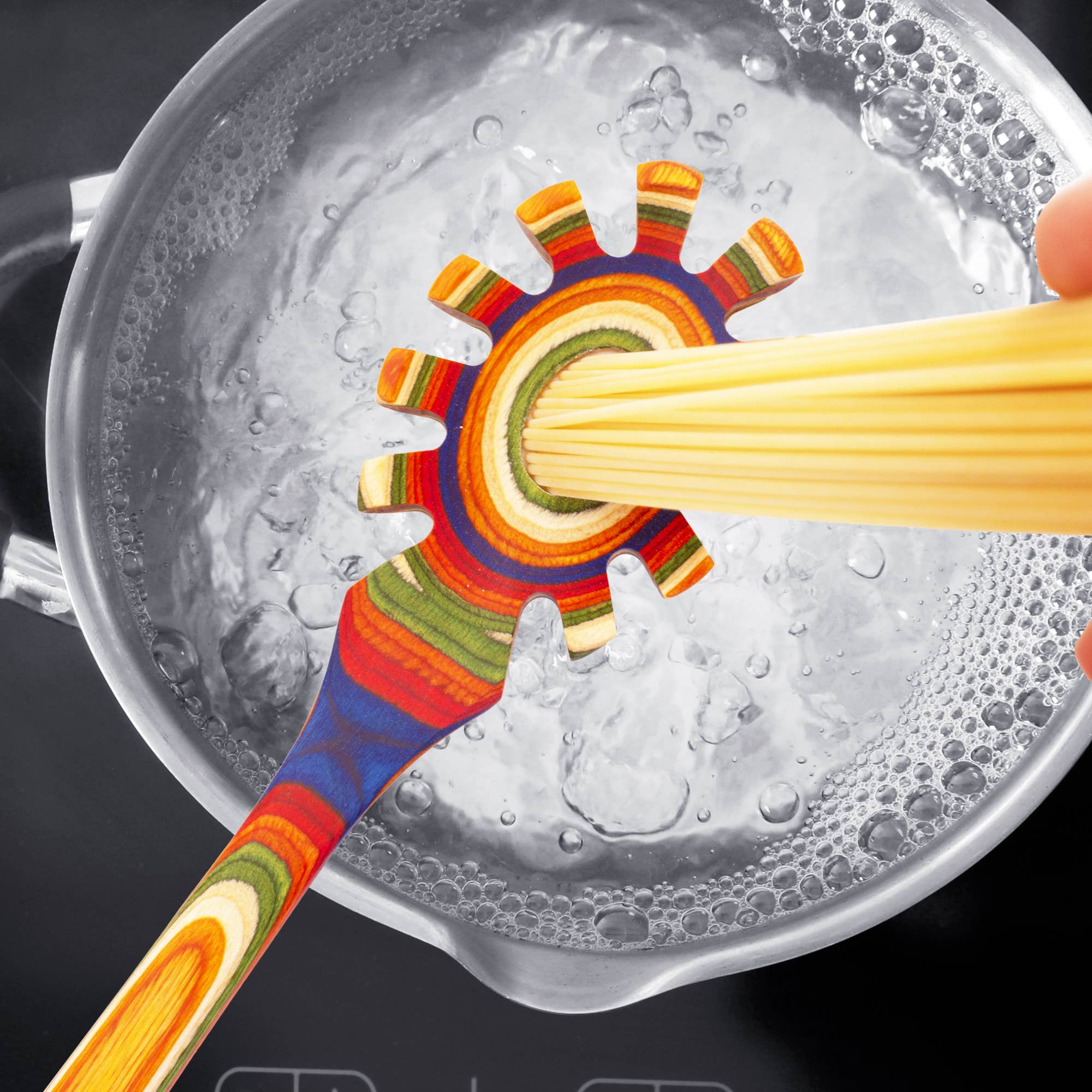 The Utensil: Marrakesh Collection Spaghetti Server, adorned with vibrant rainbow hues, gracefully holds spaghetti over a pot of boiling water on the stove.