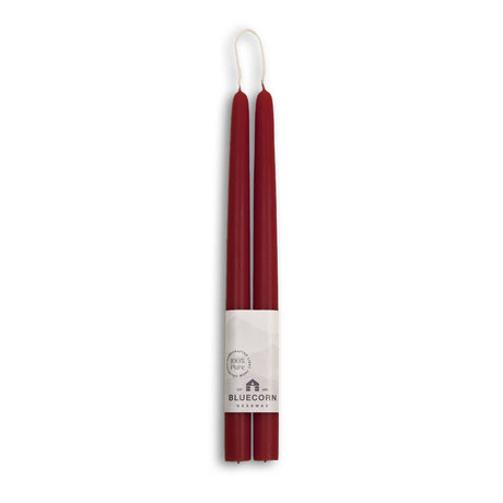 Bluecorn Beeswax offers eco-friendly, dripless taper candles; two 10-inch red beeswax candles paired in a bundle with a white brand label at the base, merging elegance and sustainability for any setting.
