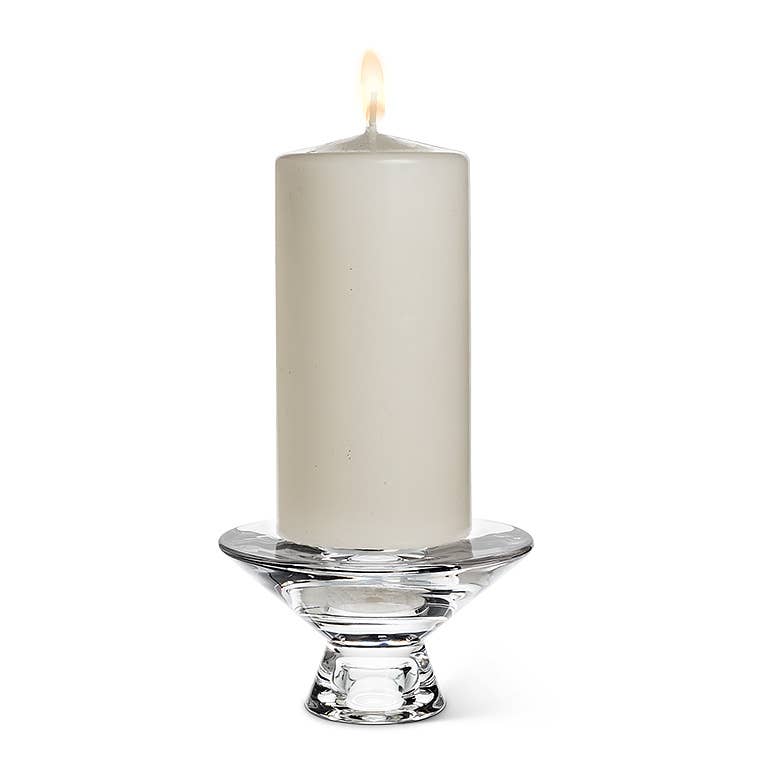 A white pillar candle lit on a Reversible Glass Candleholder (4.5" D).