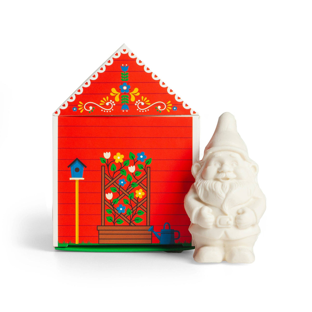 A white gnome figurine next to a red house illustration decorated with flowers, a birdhouse, and bar soap labeled “Gnome’s Cottage” on the front.