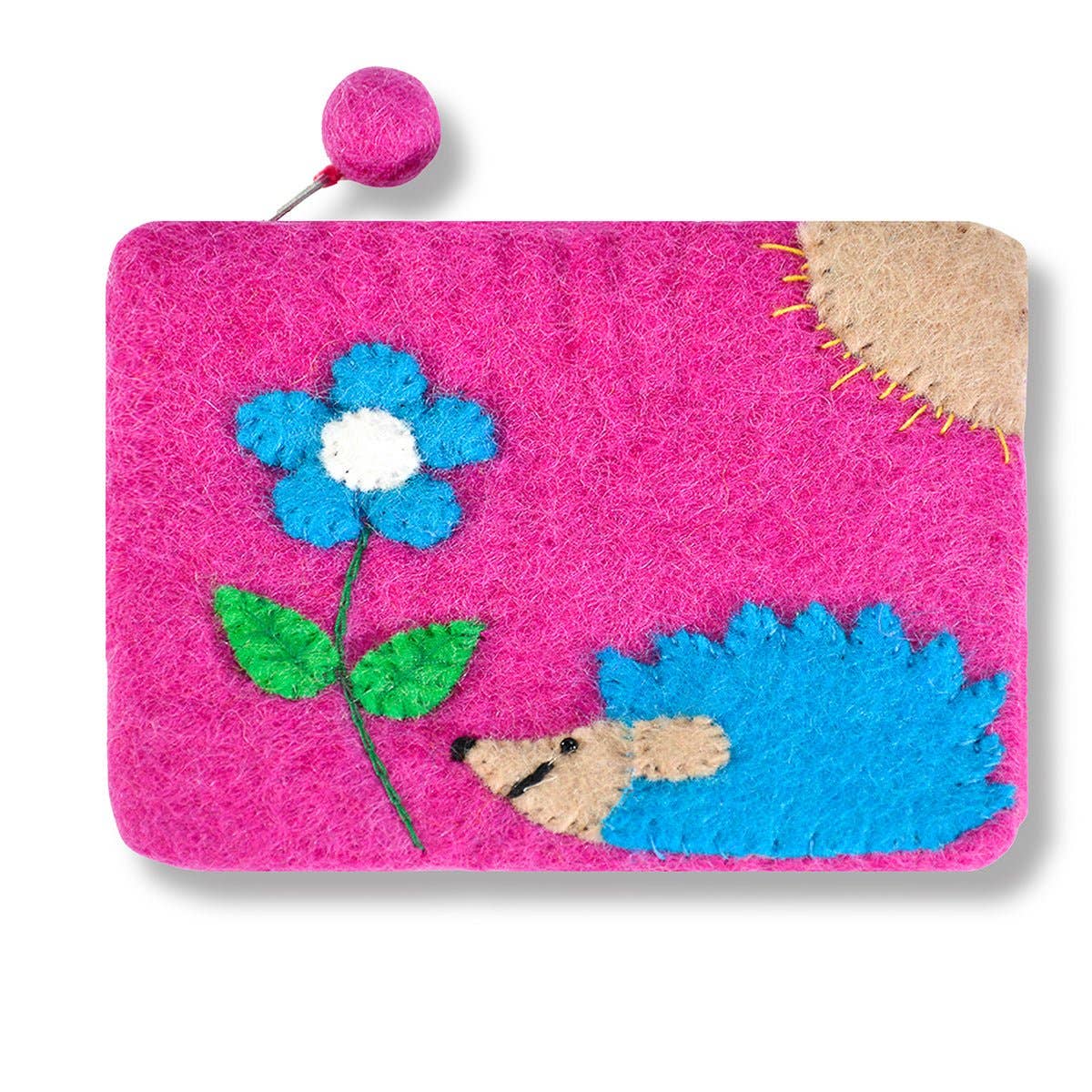 The Hedgehog and Flower Coin Purse features pink 100% wool, a blue and beige hedgehog, a blue flower, a sun accent, and a round zipper pull.