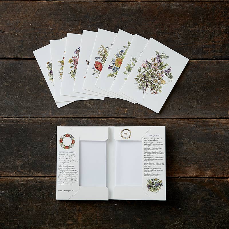 The "Bouquets - Buketter" quality greeting card pack, featuring eight floral-themed cards and eco-friendly envelopes, is elegantly spread across a wooden surface, with additional cards peeking out of an open envelope.