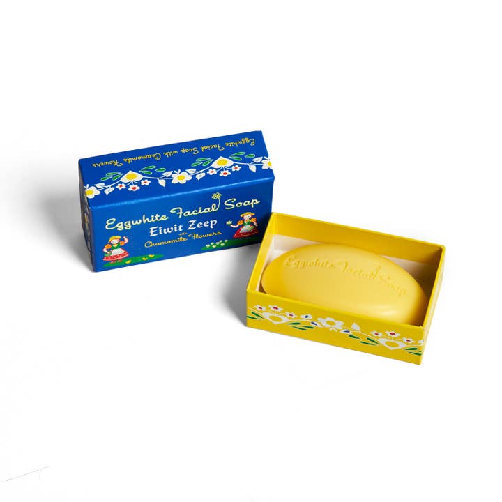 A yellow box with a bar of Soap: Eggwhite & Chamomile Facial Soap – 2.25 oz beside its blue and yellow lid—a gentle daily cleanser with chamomile for soft, refreshed skin.