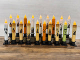 A row of Frankenstein Halloween battery-operated timer taper candles is arranged on a wooden surface.