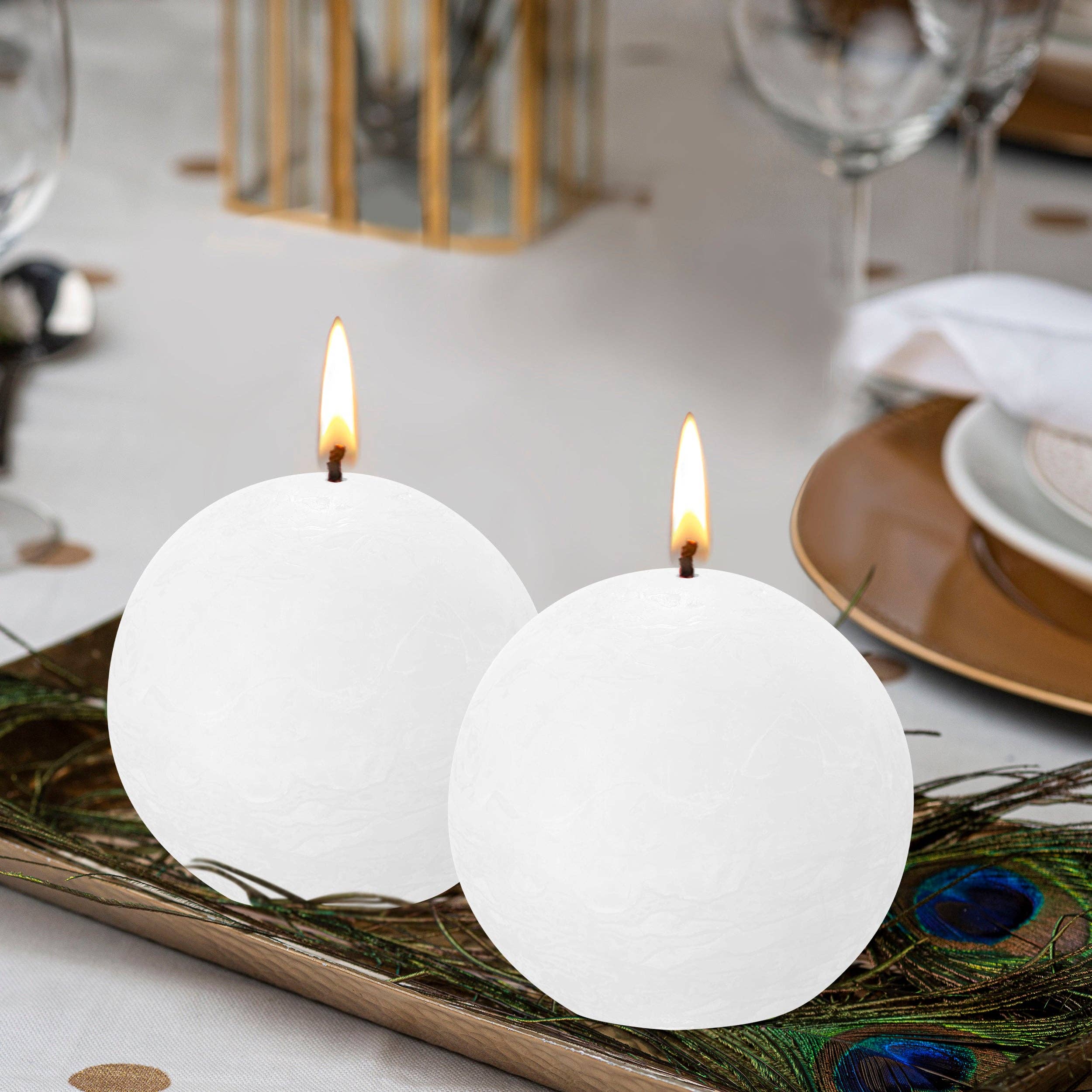 The dining table features a peacock feather tray holding two Ash Rose Rustic 3" round unscented candles made from natural, eco-friendly plant-based wax, perfectly complementing the arrangement of plates and glassware.