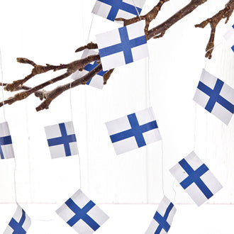 The Ornament: Finnish Flag Garland dangles charmingly like Christmas tree ornaments, adorning the tree branches against a white indoor backdrop.