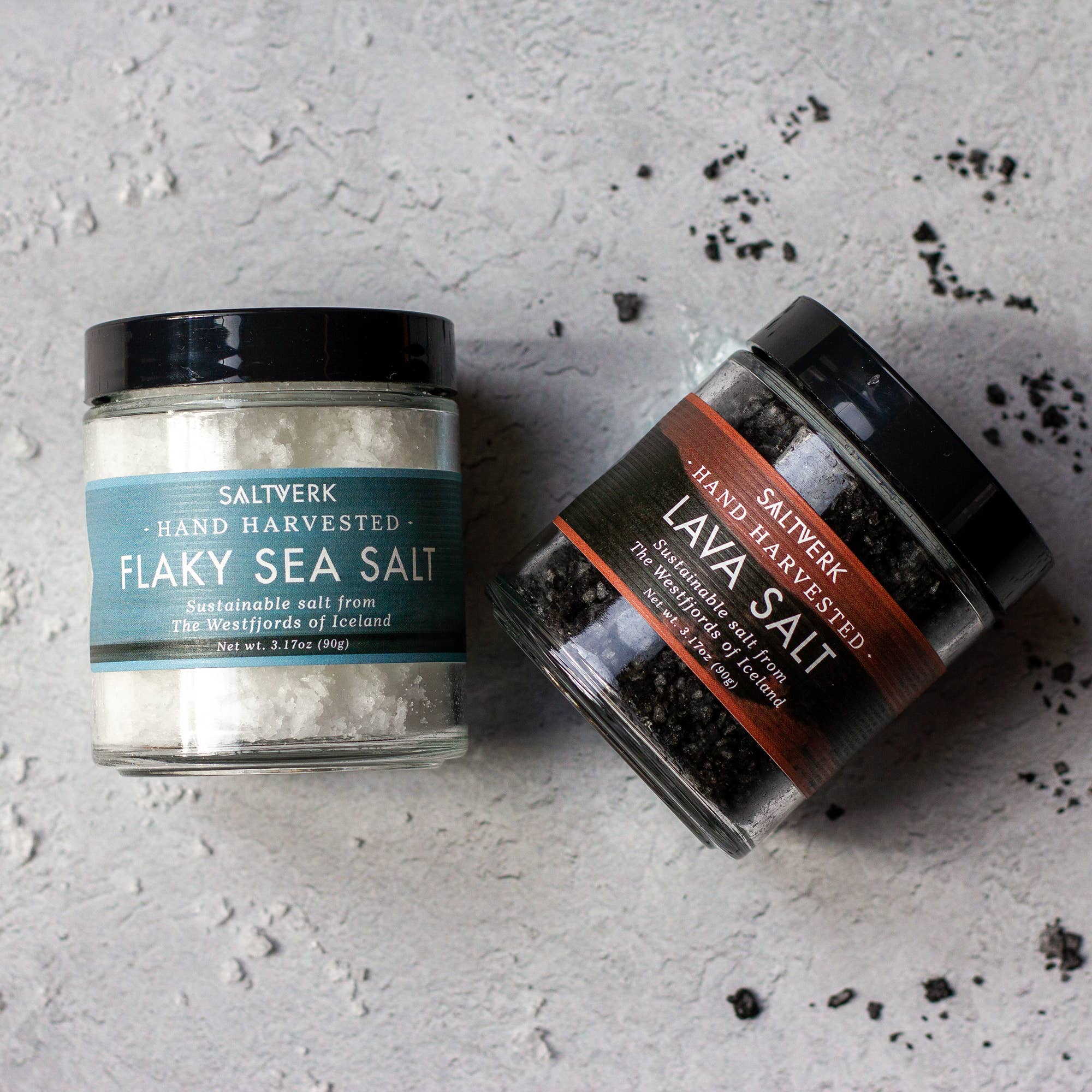 The SALTVERK Gift Set features two jars on a gray surface: one with white Flaky Sea Salt and one with striking black Lava Salt.