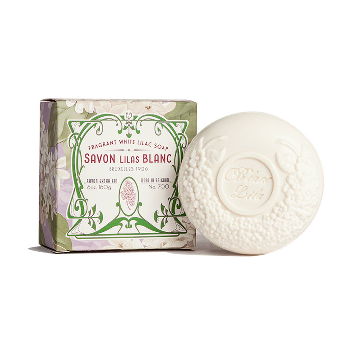 The round, white Blanc Lila Lilac Savon Bar Soap features floral embossing and is shown beside a decorative, plastic-free box with a green and lavender floral design labeled "Savon Lilas Blanc.