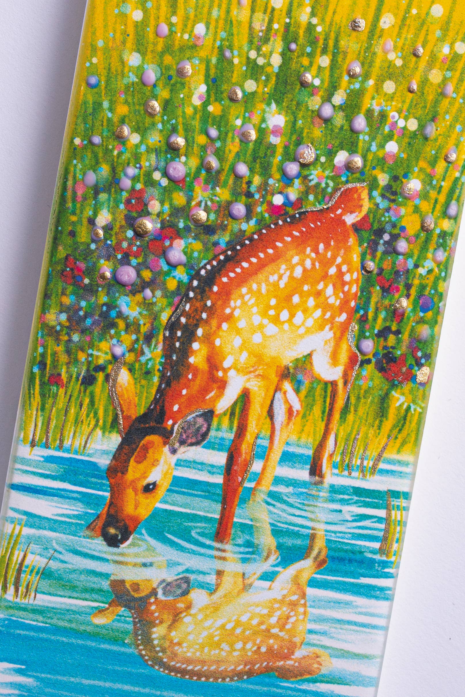 In the serene scene of a reflective pool surrounded by vibrant, dotted foliage, a deer gently sips beneath the soft light of the Deer in Meadow Pond - Flat Candle.