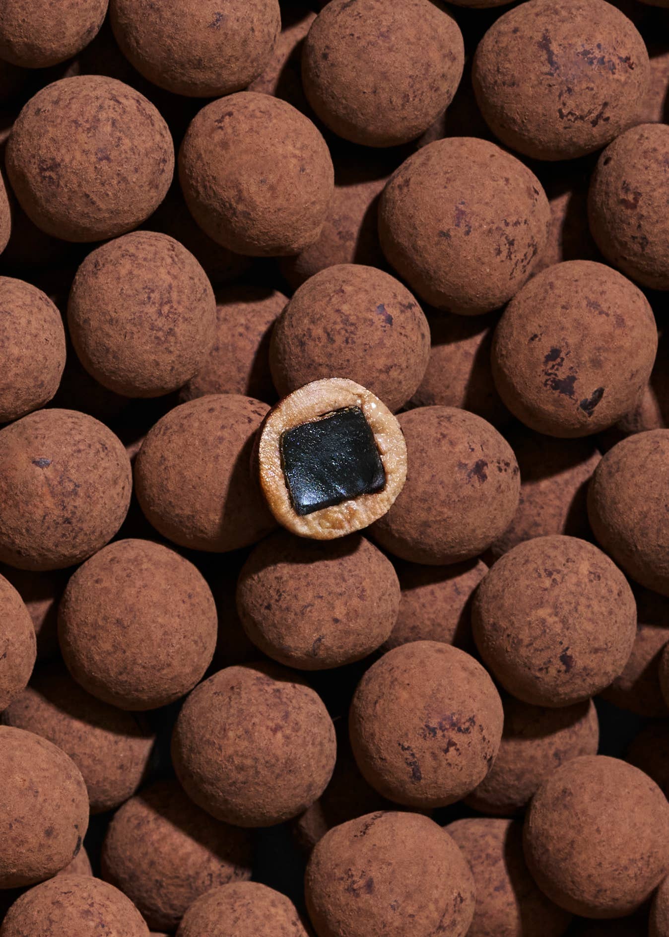 A group of round, cocoa-dusted Candy: Double Chocolate – Danish Gourmet Licorice (Small, Limited Edition) truffles, with one cut open to reveal a rich dark licorice-infused center.