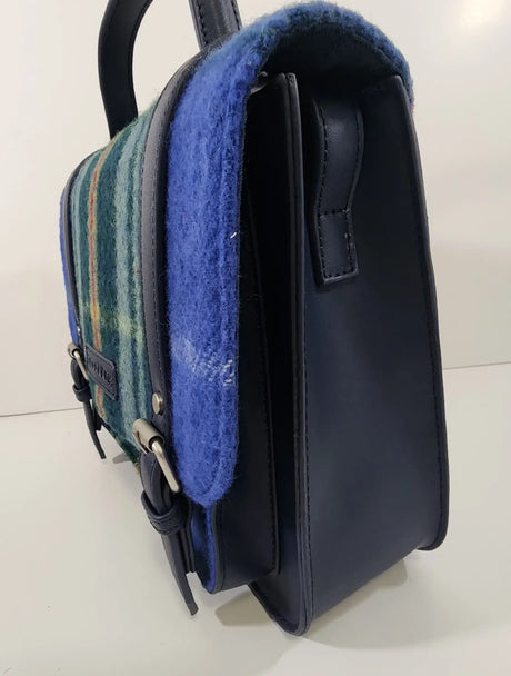 A side view of the Bag: Nova Scotia Patsy Handbag shows its structured shape, blue and green plaid fabric, blue wool trim, leather details, and top handle.