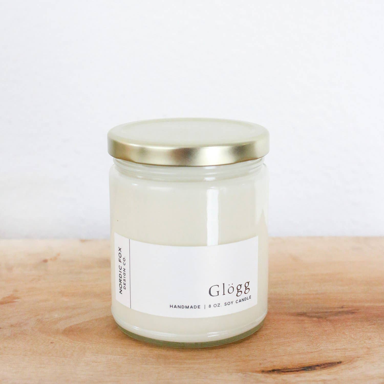The Candle: Glögg Handmade Soy Candle, 8 oz. jar, with a gold lid, inspired by Scandinavian mulled wine, sits on a wooden surface against a white backdrop.