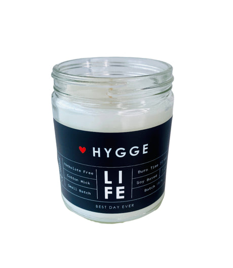 A clear glass Hygge candle with a black label reading "Hygge (Danish for comfort)," scented with Sea Salt & Orchid, made from phthalate-free soy coconut wax and a cotton wick, marked "Best Day Ever" on the bottom.