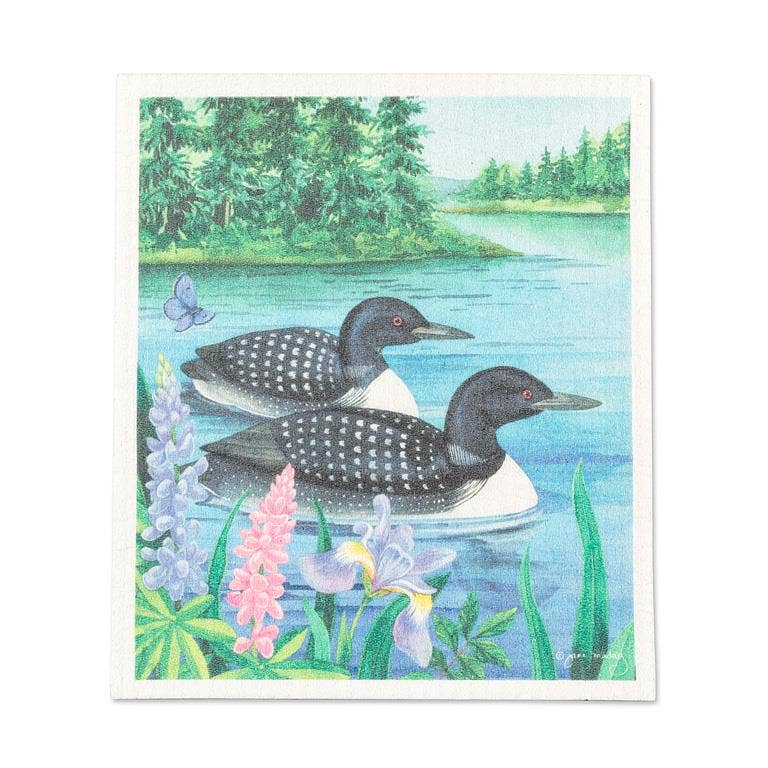 Enjoy beautiful Canadian wildlife at home with the Dish Cloth: Loon Pair on the Lake Swedish Dishcloth-6.75x7.5"L, featuring two loons swimming near a forested shore with vibrant flowers—a perfect eco-friendly addition to your kitchen.