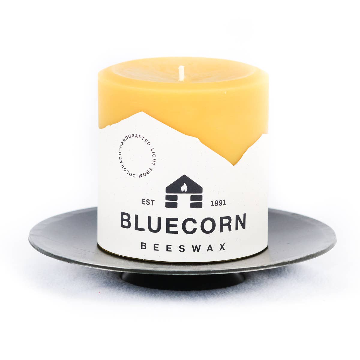 A yellow BLUECORN BEESWAX pillar candle sits on a Candle Holder: Forged Steel Pillar Candle Base (4.75" diameter) against a white background.