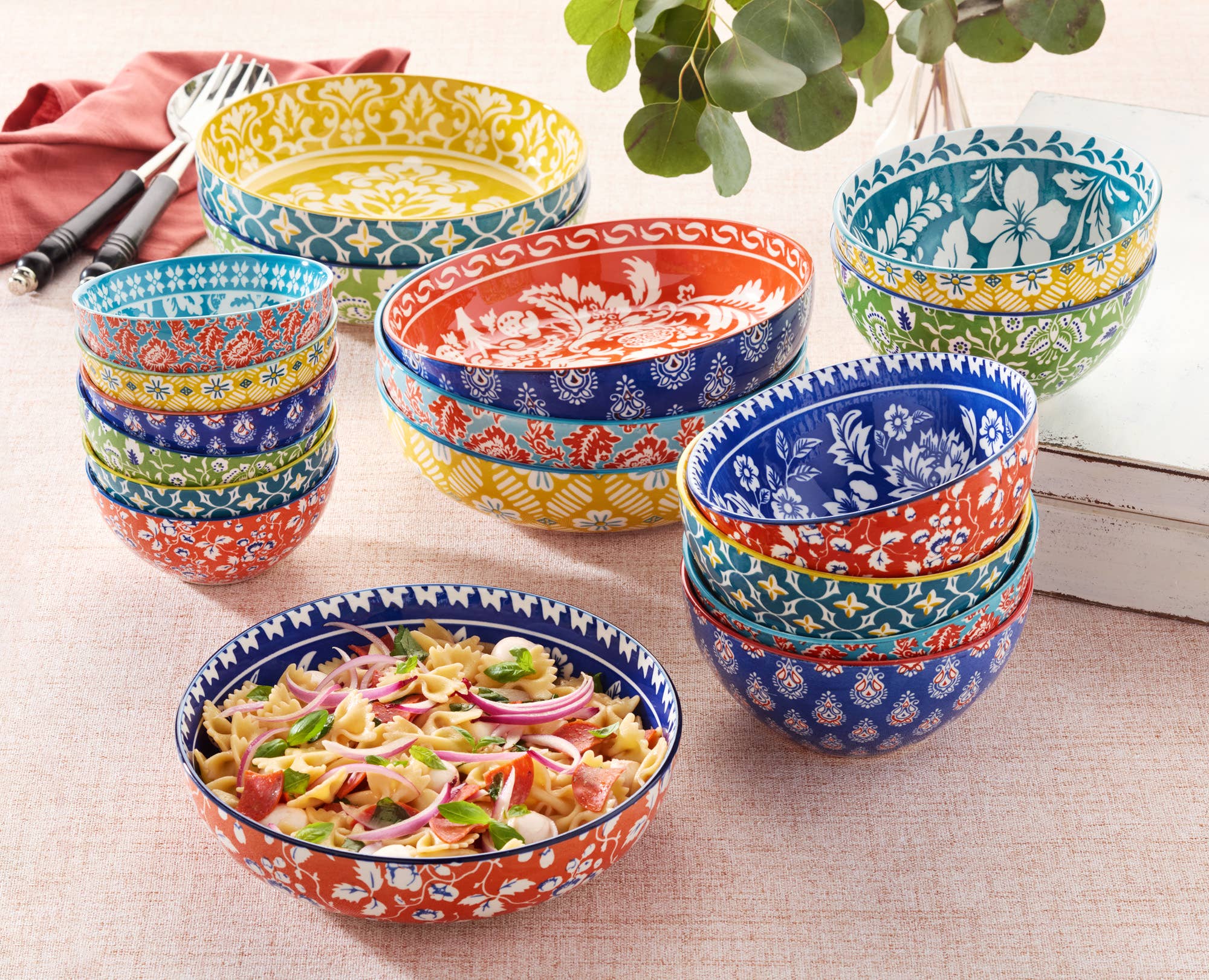 A set of six 6.25-inch Multi-Color Patterned Porcelain All Purpose Bowls are arranged on a table, with one bowl filled with pasta salad, red onions, and greens.