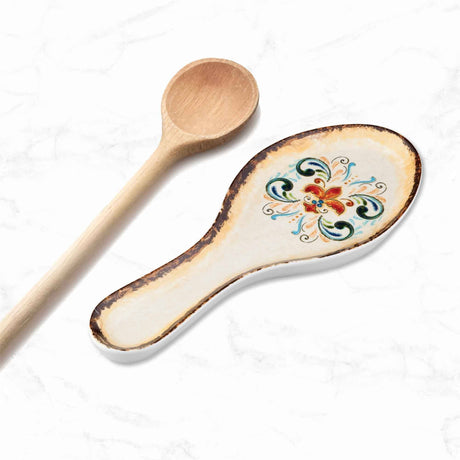 Wooden spoon next to ceramic spoon rest with folk art floral pattern, displayed on a white marbled surface.