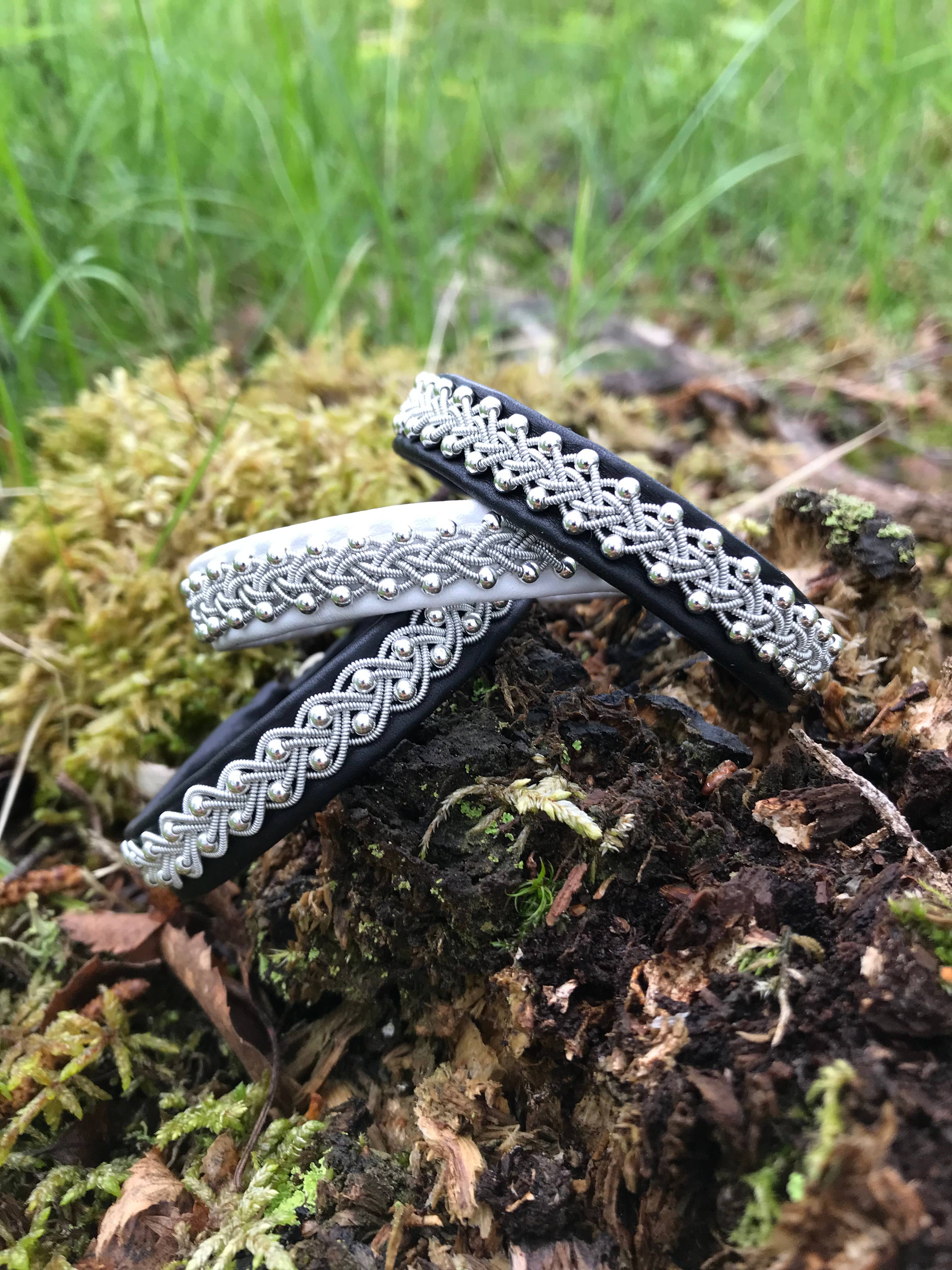 The Sami Lapland Bracelet (#39) features reindeer hide, pewter, silver, gold beads, and a black band (17-18 cm), displayed outdoors on mossy ground among grass and leaves.