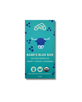 Blue chocolate bar wrapper with blue cow illustration, wild blueberries, text stating 45% milk chocolate, creamy, toasted, and visible certification icons.