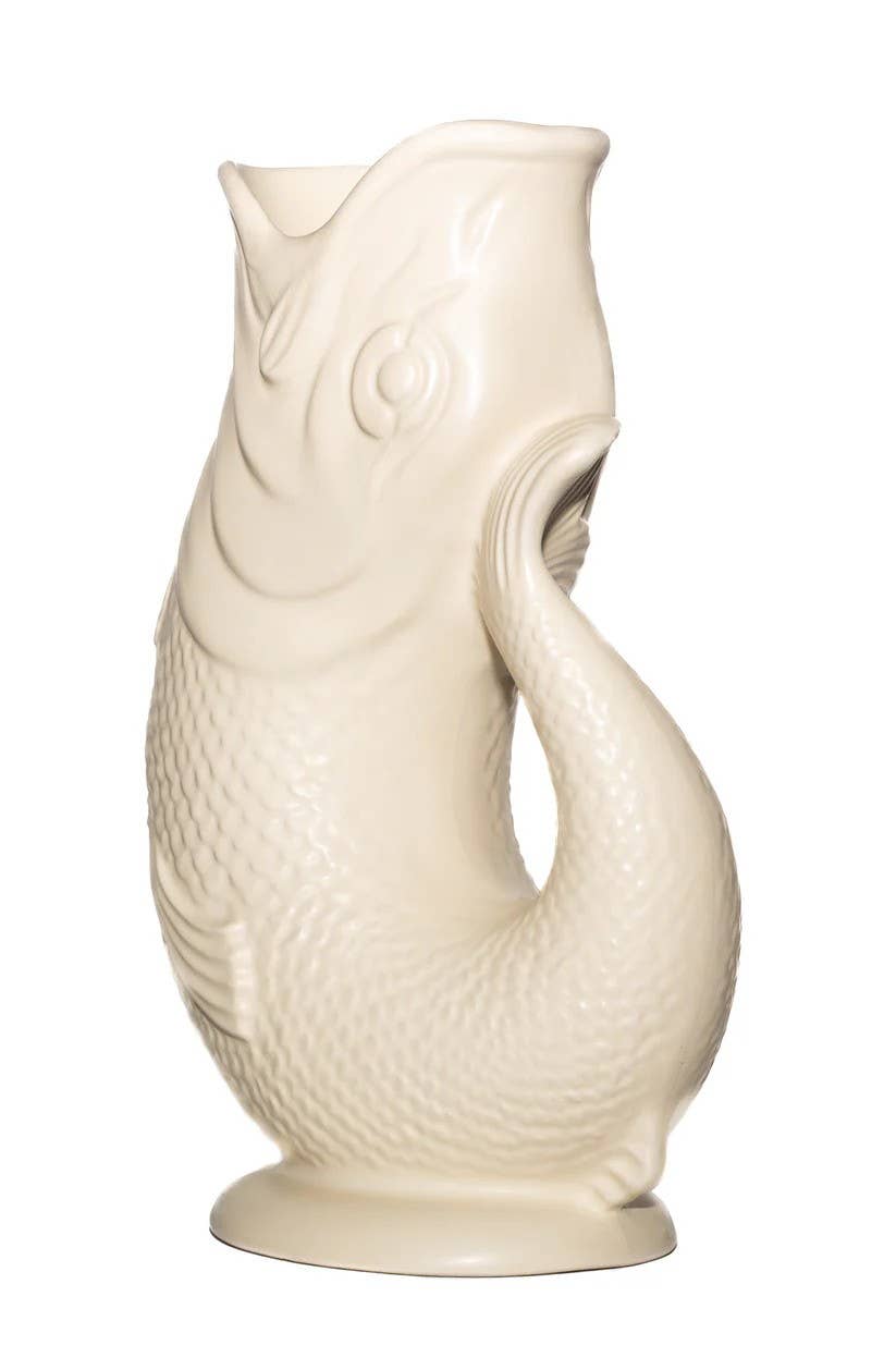 This Gluggle Jug in matt sand is a cream-colored ceramic pitcher shaped like a fish, featuring a curved tail handle and textured scale pattern, reminiscent of classic novelty dinnerware.