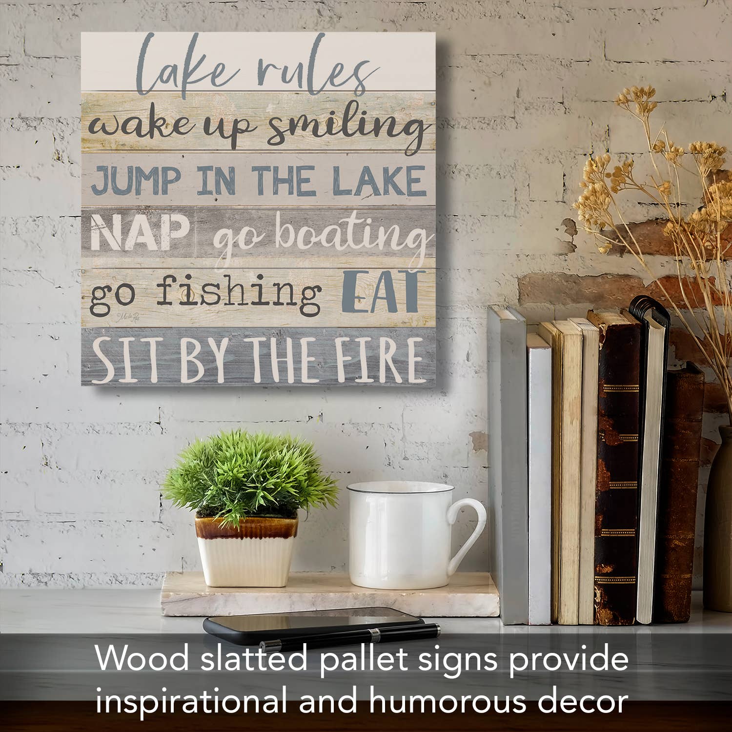 The "Lake Rules" Decorative Slatted Pallet Wood Sign, made from solid pine wood slats, brings rustic charm to your home decor as it hangs on the wall above a shelf featuring books, a plant, and a white mug.