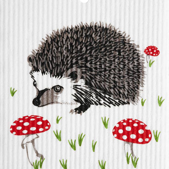 The Dish Cloth: Hedgehog with Mushrooms Swedish Wash Towel features an illustration of a hedgehog nestled among grass and three red mushrooms with white spots, capturing the essence of an eco-friendly setting.