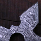 Close-up of a Damascus axe blade with detailed wavy metal patterns, placed on a dark wooden surface.