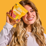 A woman with long blonde hair holds a yellow Bites of Sweden candy bag next to her face, standing against a solid yellow background.