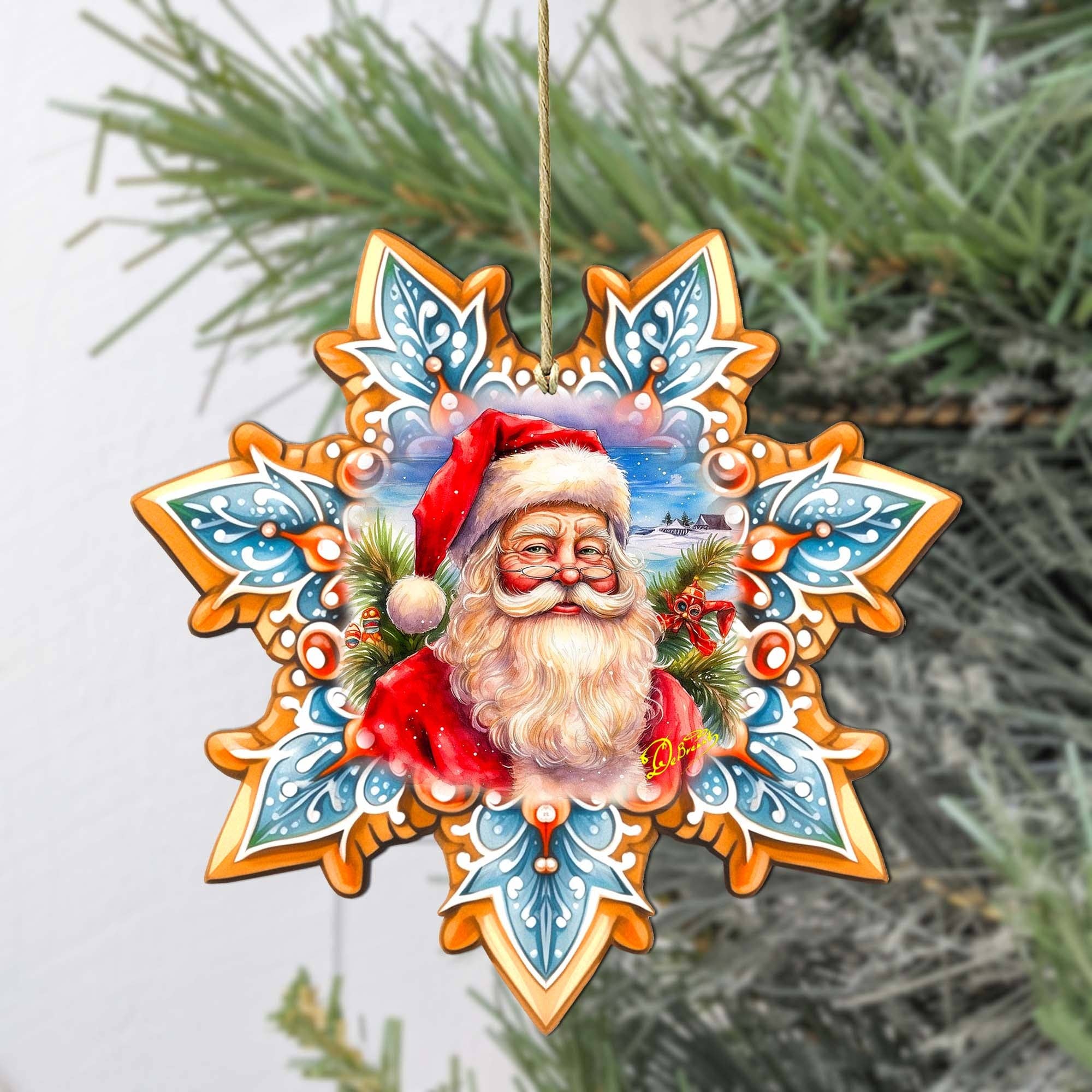 A "Santa Snowflake Wood Ornament" from the GDebrekht collection, showcasing Santa Claus in a red hat and surrounded by intricate patterns, hangs elegantly on a pine tree branch.