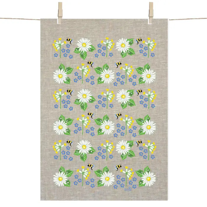 The Tea Towel: Swedish Summer Flowers Tea Towel by Anneko Design Sweden hangs on a line, displaying cheerful white daisies, yellow and blue summer flowers, green leaves, and small bees.