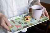 Person holding a bamboo tray featuring Dala horse and winter patterns, two jam-centered cookies, and a pale pink mug of coffee.