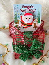 A board book with a Santa finger puppet topper, positioned inside a red and green mesh gift box ornament.