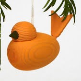 The Ornament: Orange Wooden Scandi Bird Made in Sweden features a round body and tail, inspired by Swedish tradition. Hanging from a string, it adds charming Christmas decor among green leaves.