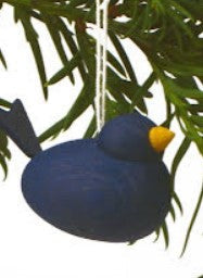 The Ornament: Wooden Scandi Bird Blue, handmade in Sweden, is a charming piece featuring a blue shape and yellow beak. It elegantly hangs from a string on a branch with green leaves, perfect as table decor.