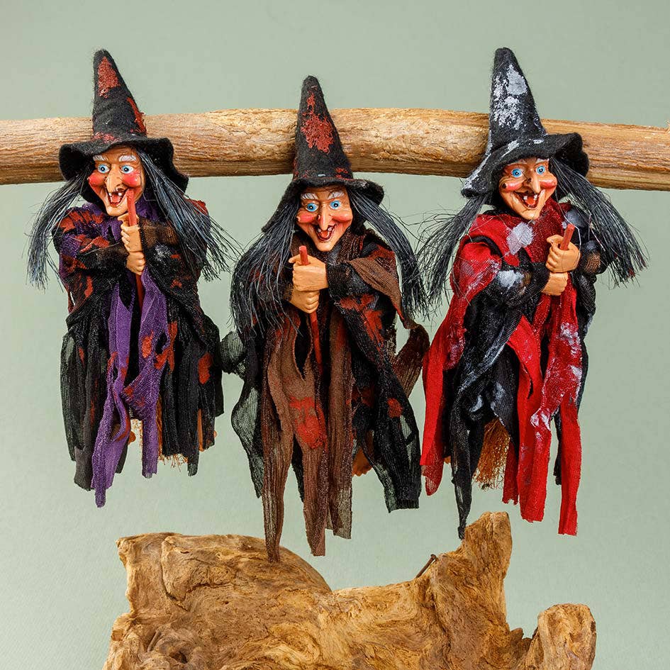 The Walburga Purple Kitchen Witch Doll is an 8" tall figurine featuring a whimsical witch in purple attire, riding a hanging broom—an enchanting good luck charm famously believed to protect kitchens.
