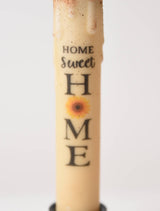 The Candle: Home Sweet Home Sunflower LED Timer Taper Candle features a cream color, sunflower image, and "Home Sweet Home" text, adding charm and convenience to your space with its top-dusted LED timer design.