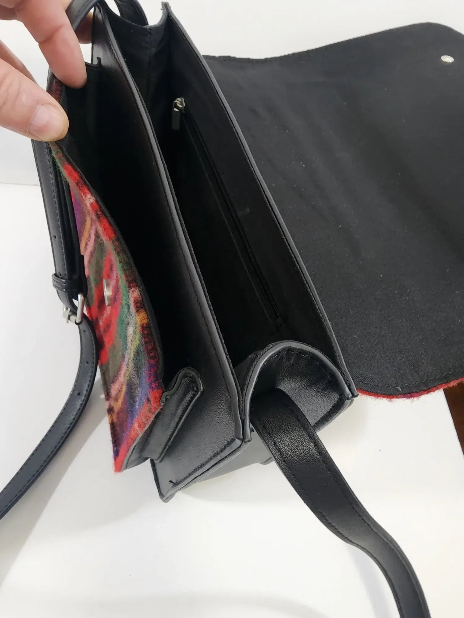 A hand holds open the Bag: Royal Stewart Handbag, featuring a black wool body with a colorful Scottish tartan flap, showing multiple compartments and a zippered pocket inside.