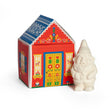 A small white gnome figurine next to a red house-shaped box with Nordic folk art patterns, containing bar soap labeled “Gnome’s Cottage.”.